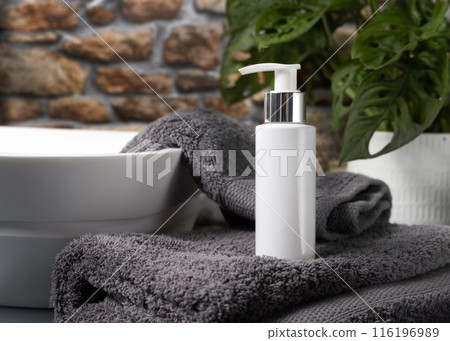White pump bottle on grey towel near basin against stone wall and green plant close up, mockup White pump bottle on grey towel near basin against stone wall and green plant close up, mockup 116196989