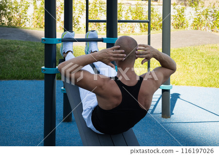 Athlete handsome male make fitness exercises and pumps up abs on street sports ground. Workouts and morning routines. Public sports field at modern city. 116197026