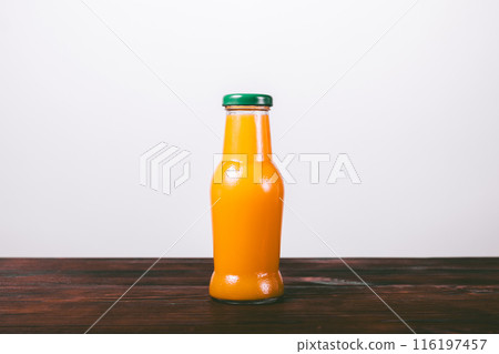 A glass bottle of orange juice is sitting on a wooden table A glass bottle of orange juice is sitting on a wooden table 116197457