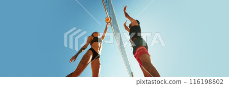 Two people playing beach volleyball, reaching for ball above t net, against clear blue sky. Banner. Active and dynamic hobby Two people playing beach volleyball, reaching for ball above t net, against clear blue sky. Banner. Active and dynamic hobby 116198802