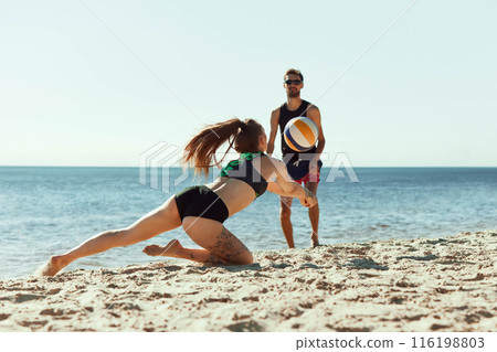 Young people, friends gathering for a game in early morning. Young man and woman play beach volleyball be the sea Young people, friends gathering for a game in early morning. Young man and woman play beach volleyball be the sea 116198803