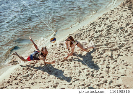 Aerial view on two young people, men and women in motion, playing beach volleyball with determination and motivation, enjoying early morning vibe Aerial view on two young people, men and women in motion, playing beach volleyball with determination and motivation, enjoying early morning vibe 116198816