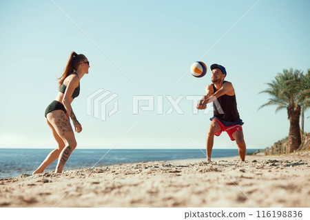 Volleyball players under the summer sun, young man and woman in motion, playing on beach in the morning, 116198836