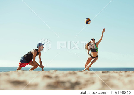 Low angle view. Concentrated young man and woman in sportswear in motion, play in beach volleyball under sunny clear sky. Low angle view. Concentrated young man and woman in sportswear in motion, play in beach volleyball under sunny clear sky. 116198840