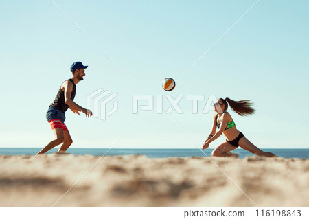 Energetic beach volleyball scene with a man and woman competing under the summer sun. Dynamic image of young man and woman Energetic beach volleyball scene with a man and woman competing under the summer sun. Dynamic image of young man and woman 116198843