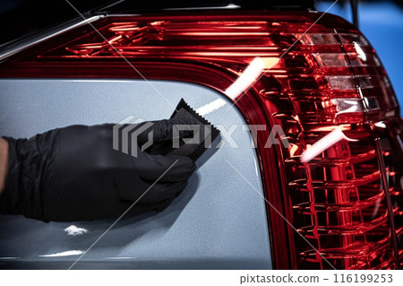 Mechanic wearing black gloves applying a ceramic coating to a car surface in a detailing studio 116199253