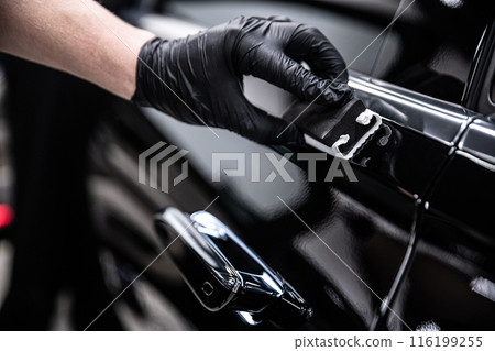 Mechanic wearing black gloves applying a ceramic coating to a car door handle in a detailing studio 116199255