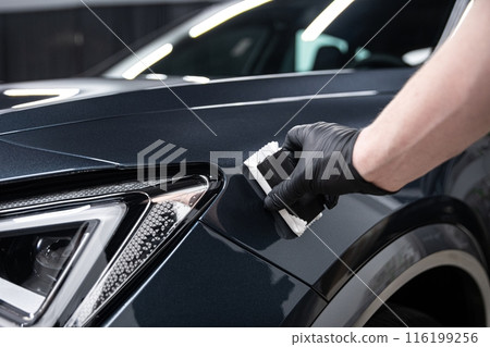 Mechanic wearing black gloves applying a protective coating to a car's front fender in a detailing studio Mechanic wearing black gloves applying a protective coating to a car's front fender in a detailing studio 116199256