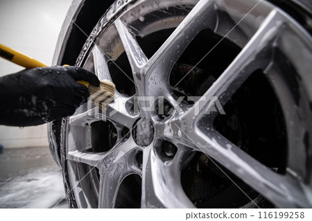Mechanic wearing black gloves cleaning a car wheel with a brush in a detailing studio Mechanic wearing black gloves cleaning a car wheel with a brush in a detailing studio 116199258