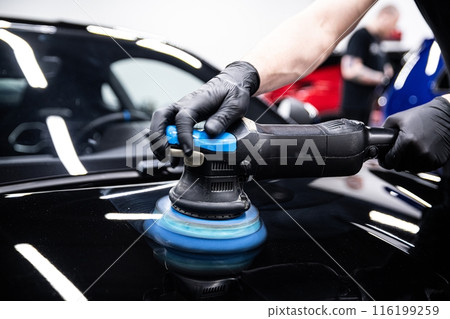 Mechanic wearing black gloves polishing car paint with a machine in a detailing studio. 116199259