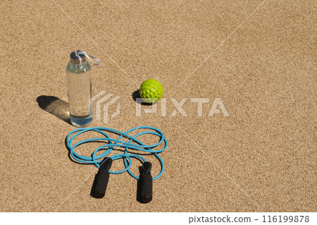 Sports fitness equipment. Set of water, jump rope and massage ball for workout and activity on outdoor sports ground. Copy space. Sports fitness equipment. Set of water, jump rope and massage ball for workout and activity on outdoor sports ground. Copy space. 116199878
