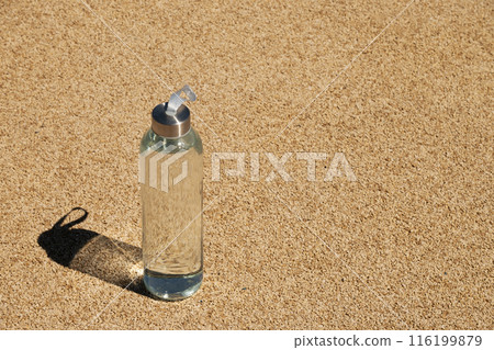 Transparent refreshing glass bottle of water in sunny day with hard shadow on outdoor beige sports ground with artificial covering. Concept water balance for heat season for workout. View from above Transparent refreshing glass bottle of water in sunny day with hard shadow on outdoor beige sports ground with artificial covering. Concept water balance for heat season for workout. View from above 116199879