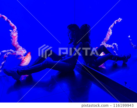 A girl in an aquarium against the background of floating jellyfish in a colourful aquarium 116199943