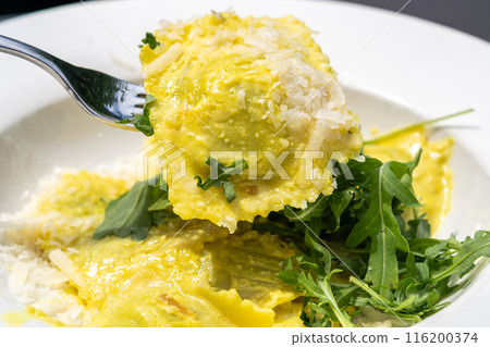 Ravioli, stuffed pasta filled with cheese, arugula topped, grated cheese, served in a lemon zest sauce 116200374