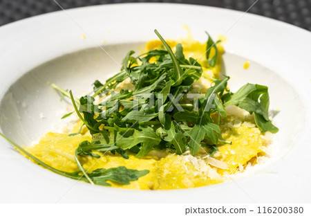 Ravioli, stuffed pasta filled with cheese, arugula topped, grated cheese, served in a lemon zest sauce 116200380