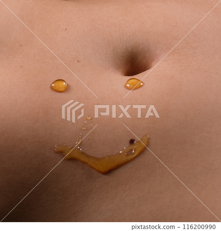 Beautiful seductive young female makes a honey on a black background. Drops of honey on her belly. 116200990
