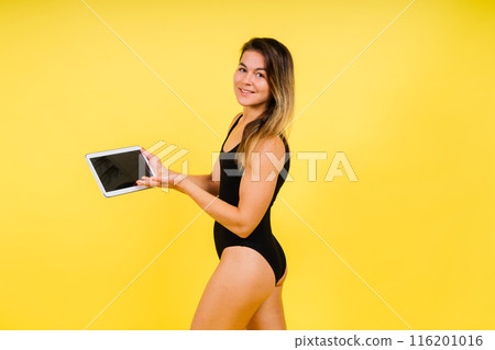 Female dressed in a bodysuit on a yellow background in studio with tablet laptop Female dressed in a bodysuit on a yellow background in studio with tablet laptop 116201016