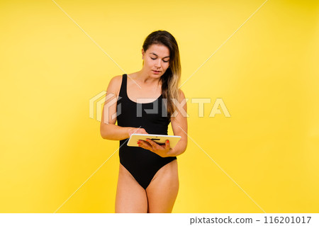 Female dressed in a bodysuit on a yellow background in studio with tablet laptop Female dressed in a bodysuit on a yellow background in studio with tablet laptop 116201017