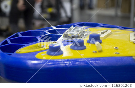 Musical instrument guitar 3D printed from molten plastic in yellow and blue colors. Part of guitar created by 3D printing from yellow-blue plastic. Concept 3D printer 3D printing modeling prototyping Musical instrument guitar 3D printed from molten plastic in yellow and blue colors. Part of guitar created by 3D printing from yellow-blue plastic. Concept 3D printer 3D printing modeling prototyping 116201268