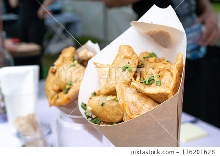 Fried dumplings samosas in paper cones, street food stall, savory snack chopped herbs, crispy deep-fried dumplings Fried dumplings samosas in paper cones, street food stall, savory snack chopped herbs, crispy deep-fried dumplings 116201628