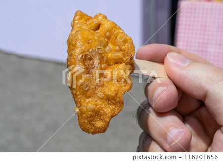 Fried dumpling, samosa on stick, handheld snack, golden crispy texture, deep-fried goodness in hand 116201656