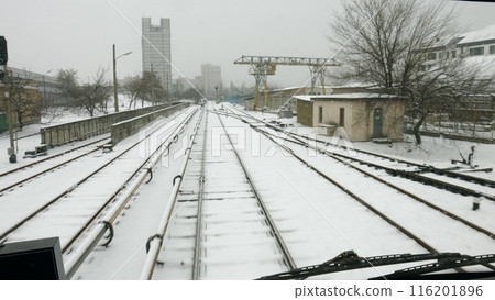 Winter at the railway station. Train goes through the industrial zone to the station. 116201896