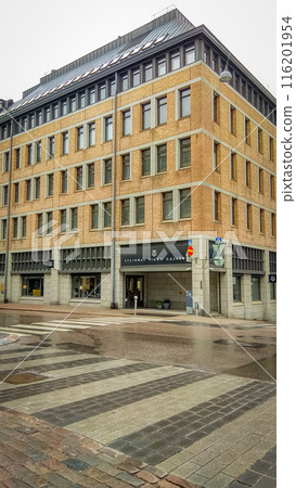 Orange brick building corner of Steinway Piano Gallery in Helsinki bottom up view from wet road with road crossing Orange brick building corner of Steinway Piano Gallery in Helsinki bottom up view from wet road with road crossing 116201954