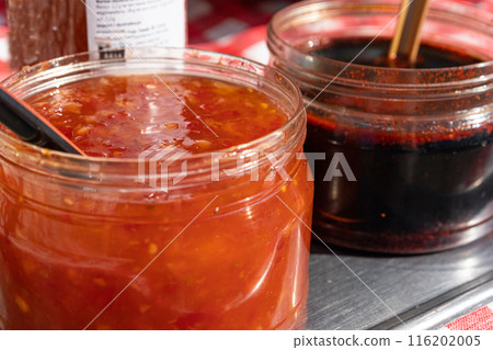 Two jars with red and dark sauces on a metal table, with spoons. Chunky, spicy red sauce and dark Two jars with red and dark sauces on a metal table, with spoons. Chunky, spicy red sauce and dark 116202005