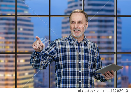 Portrait of cheerful aged man with tablet pc. Checkered night cityscape background. 116202040