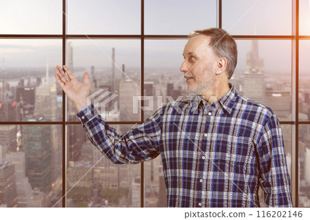 Handsome mature senior man presenting copy space with his hand. Checkered windows background with cityscape view. 116202146