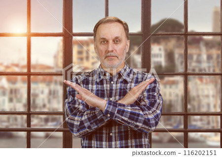 Portrait of a handsome serious man shows reject gesture with arms cross. Checkered windows backgorund with evening sunlight. 116202151