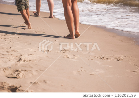 The legs of the whole family are running along the seashore and copy space. summer sea background. The legs of the whole family are running along the seashore and copy space. summer sea background. 116202159