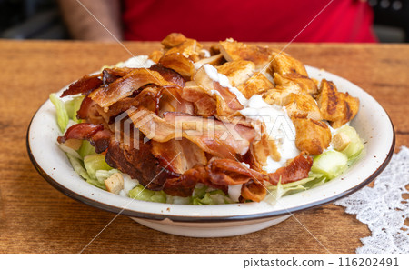 Polish Caesar salad with chicken, bacon and vegetables, high-calorie meat salad with fresh vegetables Polish Caesar salad with chicken, bacon and vegetables, high-calorie meat salad with fresh vegetables 116202491