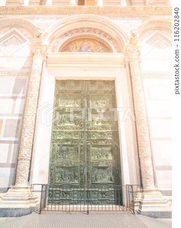 The ornate bronze doors of Pisa Cathedral, Tuscany, Italy, are framed by a white marble archway. 116202840