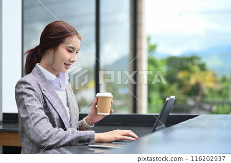 Attractive Asian female office worker holding a cup of coffee and using digital tablet at building terrace Attractive Asian female office worker holding a cup of coffee and using digital tablet at building terrace 116202937