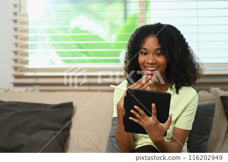 Pretty young Afro woman looking at digital tablet with surprised face 116202949