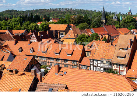 Scenic panoramic view traditional shingle tiled red rooftop old ancient medieval european german small town Quedlinburg church against blue sky background. Unesco heritage list travel destination 116203290