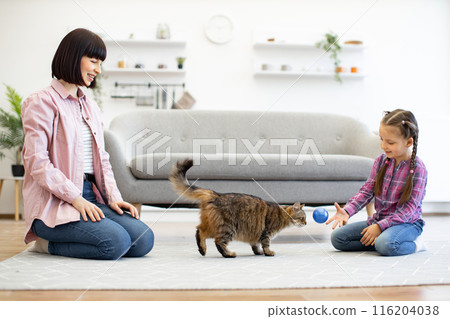 Mother and daughter playing with cat in living room 116204038