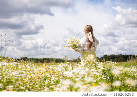 a girl in a white dress walks in a chamomile field with daisies 116206298