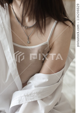 Close-up of Young woman in lingerie and white shirt sit on bed indoors at home in the morning after waking up, back view. Relaxing , Cozy, good morning, comfort, intimacy concept. 116208829