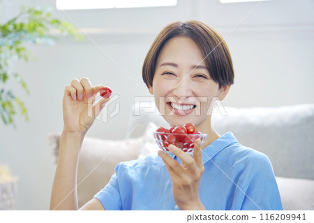 Woman eating cherry tomatoes at home looking at camera Woman eating cherry tomatoes at home looking at camera 116209941