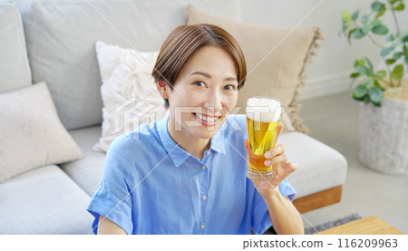 Woman drinking draft beer at home, looking at camera Woman drinking draft beer at home, looking at camera 116209963