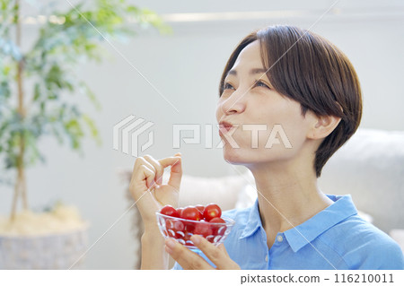 Woman eating cherry tomatoes at home 116210011