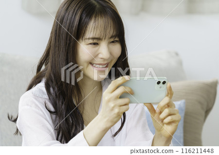 微笑的年輕女子在客廳觀看視頻，視訊通話 116211448