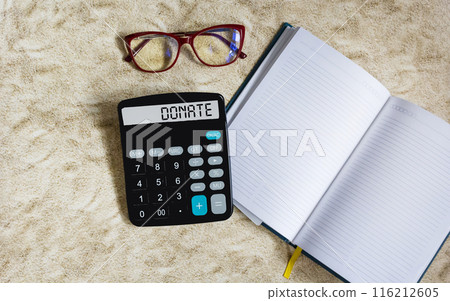 The word DONATE written on a calculator display and a light background with a notepad for writing 116212605
