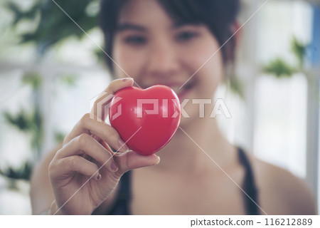 Happiness Young women hands holding red heart smile face life wellbeing symbol. Asian women's health care heart disease. Beautiful female in sportswear training fitness relaxation. Woman home fitness Happiness Young women hands holding red heart smile face life wellbeing symbol. Asian women's health care heart disease. Beautiful female in sportswear training fitness relaxation. Woman home fitness 116212889