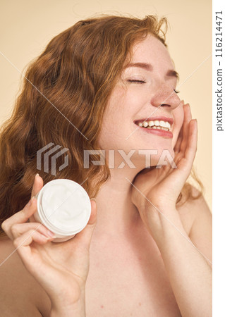 Woman Holding Skincare Cream and Smiling Radiantly with Closed Eyes 116214471