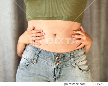 Close up of woman in jeans and green top with childs hands around her waist. Concept of family bonding, motherhood, postpartum recovery and affection. Neutral background 116215730