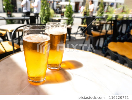 Beer glass in sunny day, cold pint glass with remaining beer on outdoor table, cool condensation Beer glass in sunny day, cold pint glass with remaining beer on outdoor table, cool condensation 116220751
