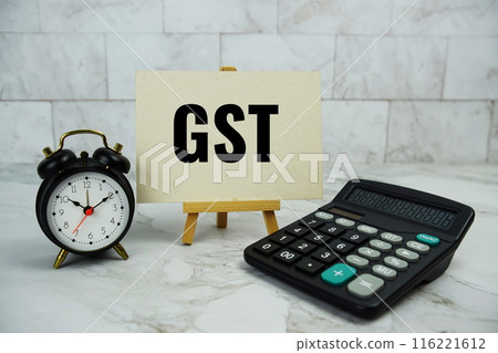 GST, goods and services tax text written on paper card with calculator and alarm clock on marble background GST, goods and services tax text written on paper card with calculator and alarm clock on marble background 116221612